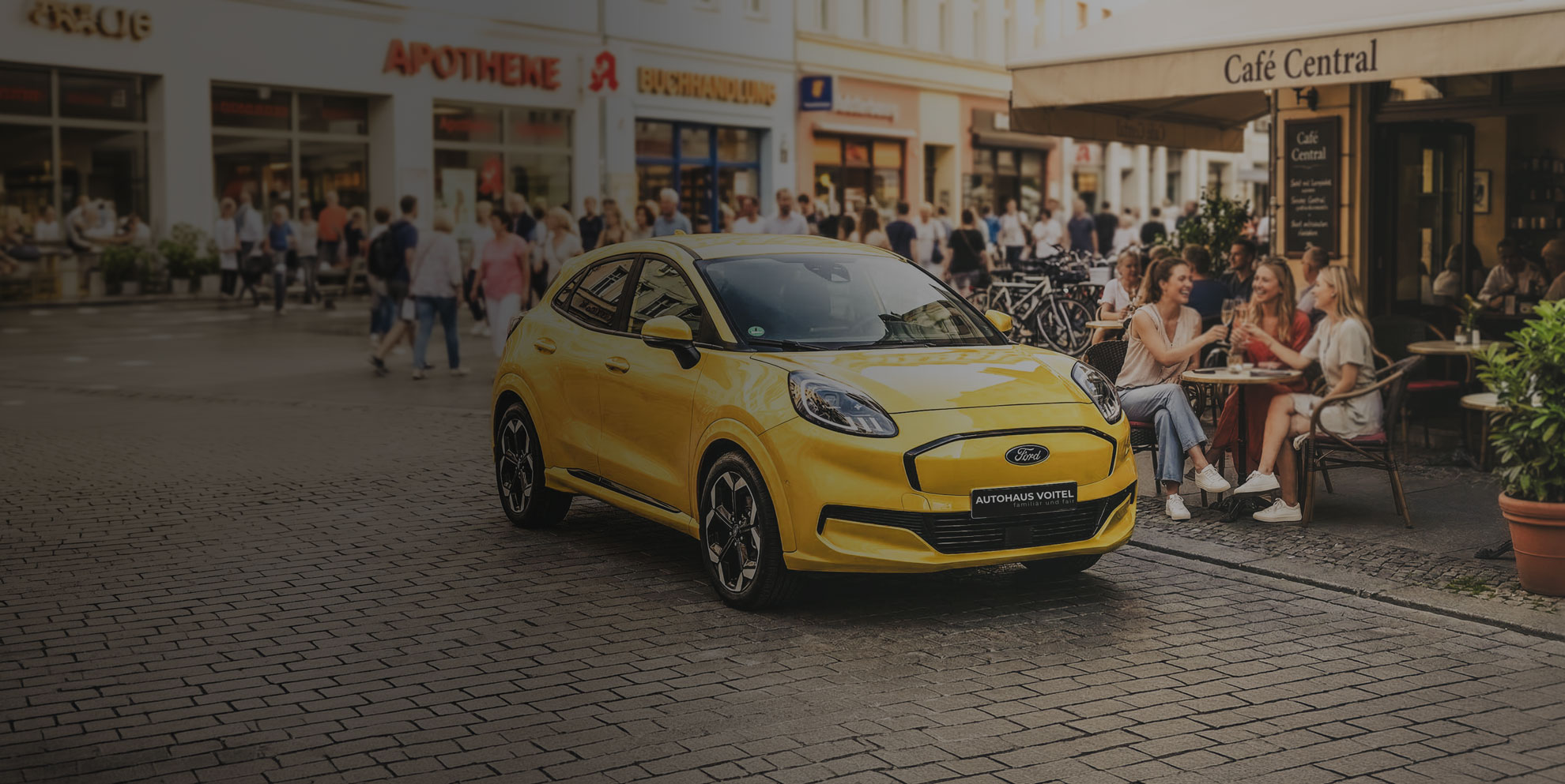 Gelber Ford Puma Gen-E von Autohaus Voitel in einer Fußgängerzone vor einem Café
